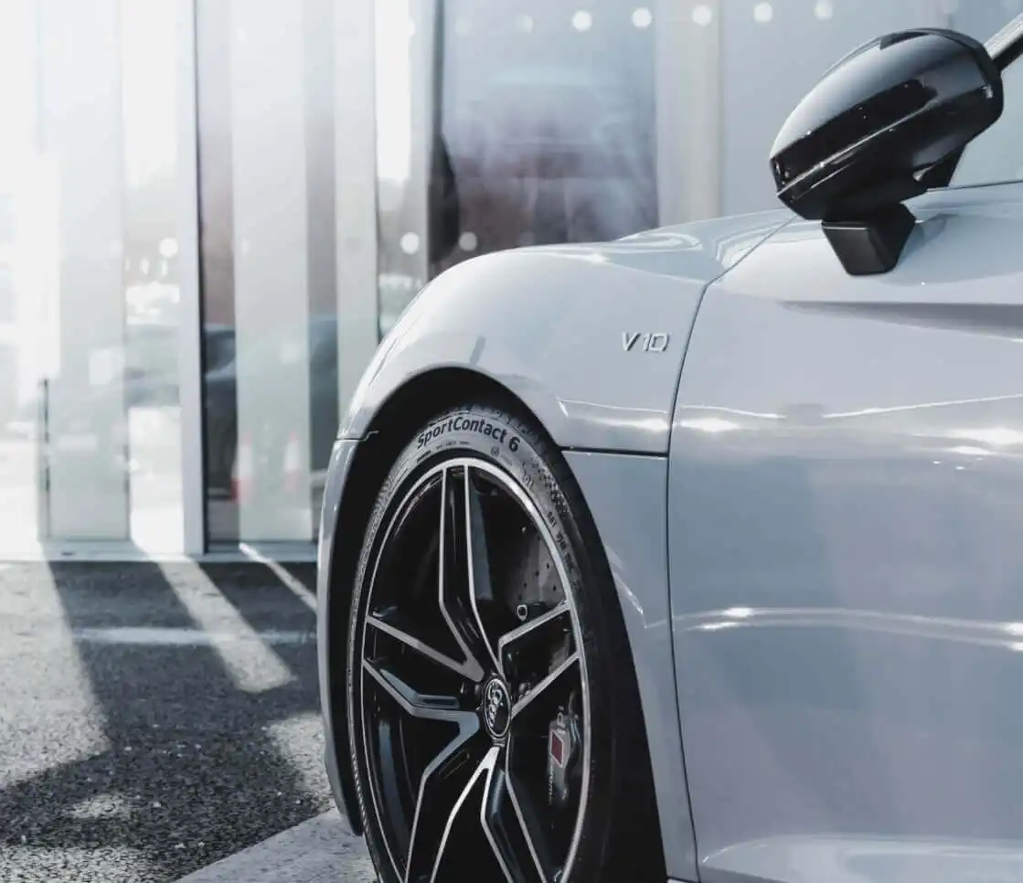 Vorderrad und Kotflügel eines grauen Audi mit V10-Schriftzug vor einem Autohaus